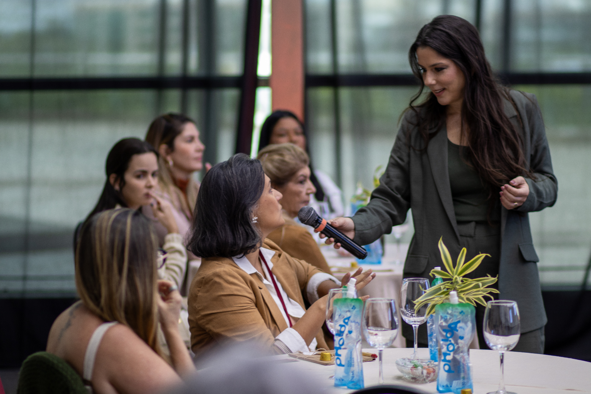 Renata André conduzindo palestra ao vivo, com microfone em mão, interagindo com mulheres da plateia